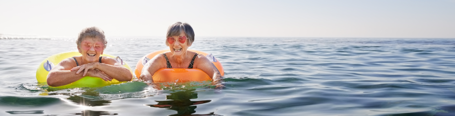Two elderly women wearing pink sunglasses and floating in tubes on the ocean