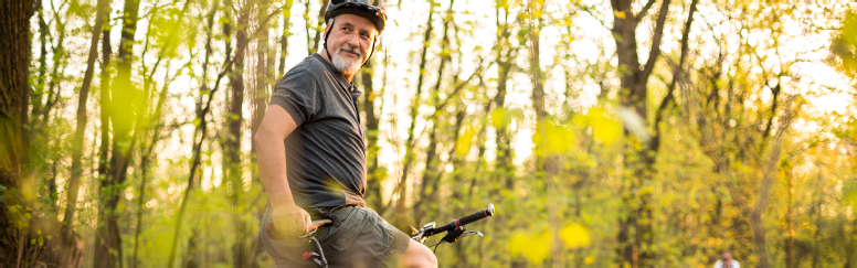 An older man wearing a helmet and riding a bicycle in the woods